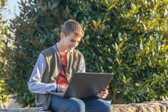 Menino alegre do adolescente com o portátil e os livros de texto que fazem trabalhos de casa e que preparam-se para um exame no p imagens de stock royalty free Menino alegre do adolescente com o portátil e os livros de texto que fazem trabalhos de casa e que preparam-se para um exame no p imagens de stock royalty free
