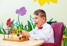 Menino bonito, criança na cadeira de rodas que resolve o enigma lógico no centro de reabilitação para crianças com necessidades e imagem de stock Menino bonito, criança na cadeira de rodas que resolve o enigma lógico no centro de reabilitação para crianças com necessidades e imagem de stock