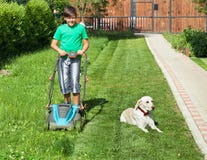 Menino que empurra um lawnmower através da jarda - acompanhada da sua faça imagens de stock royalty free Menino que empurra um lawnmower através da jarda - acompanhada da sua faça imagens de stock royalty free