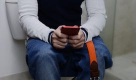 Mens in de badkamers die, die op het toilet zitten en op zijn celtelefoon letten stock afbeeldingen Mens in de badkamers die, die op het toilet zitten en op zijn celtelefoon letten stock afbeeldingen