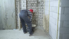 Mens die in het werkslijtage en rood GLB geluchte concrete blokmuur pleisteren stock footage Mens die in het werkslijtage en rood GLB geluchte concrete blokmuur pleisteren stock footage