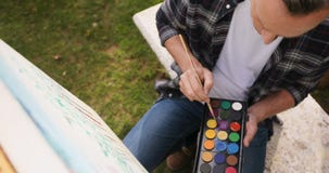 Mens het schilderen op canvas in de tuin 4k stock footage Mens het schilderen op canvas in de tuin 4k stock footage