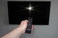 Menschliche Hand mit einer Fernbedienung vor einem schwarzen Fernseheis stockfoto Menschliche Hand mit einer Fernbedienung vor einem schwarzen Fernseheis stockfoto