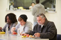 Mensen die bij Lijst zitten die Voedsel in Dakloze Schuilplaats eten royalty-vrije stock afbeeldingen Mensen die bij Lijst zitten die Voedsel in Dakloze Schuilplaats eten royalty-vrije stock afbeeldingen
