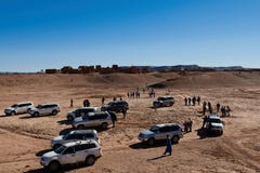 Merzouga,摩洛哥- 2018年12月05日:游人牧群在沙漠中间的有一小镇的在背景中 免版税库存照片 Merzouga,摩洛哥- 2018年12月05日:游人牧群在沙漠中间的有一小镇的在背景中 免版税库存照片
