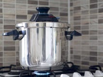 Metallic steel pressure cooker standing on the oven in the kitchen and cooking being cooked royalty free stock photography Metallic steel pressure cooker standing on the oven in the kitchen and cooking being cooked royalty free stock photography
