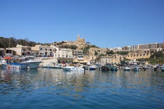 Mgarr, Мальта - май 2018: Взгляд Mgarr паромного терминала Gozo Залив с яхтами на переднем плане и старый город с церковью на вер стоковое изображение Mgarr, Мальта - май 2018: Взгляд Mgarr паромного терминала Gozo Залив с яхтами на переднем плане и старый город с церковью на вер стоковое изображение