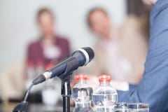 Microfoon in nadruk tegen vage mensen bij ronde tafelgebeurtenis Royalty-vrije Stock Afbeeldingen Microfoon in nadruk tegen vage mensen bij ronde tafelgebeurtenis Royalty-vrije Stock Afbeeldingen