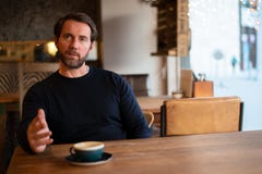 Midden oude Kaukasische mannelijke zitting bij de lijst in koffiewinkel die materiaal verklaren stock afbeeldingen Midden oude Kaukasische mannelijke zitting bij de lijst in koffiewinkel die materiaal verklaren stock afbeeldingen