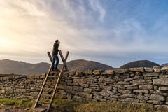 Middenleeftijdsmens die zich op de ladder op de steenmuur bevinden in bergen, die omhoog in de afstand, zonsondergang in het berg stock foto's Middenleeftijdsmens die zich op de ladder op de steenmuur bevinden in bergen, die omhoog in de afstand, zonsondergang in het berg stock foto's