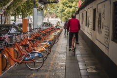 A middle-aged man in a red shirt rides a shared bicycle through a shared bicycle parking spot