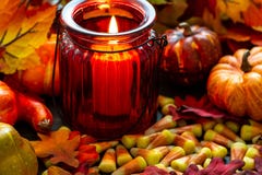 Milho de doces um deleite de Dia das Bruxas em uma tabela de madeira com um castiçal de vidro vermelho que faz os incandescer na imagem de stock Milho de doces um deleite de Dia das Bruxas em uma tabela de madeira com um castiçal de vidro vermelho que faz os incandescer na imagem de stock
