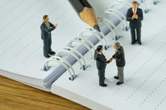 Miniature people with businessmen handshaking and others clapping on white note and pencil as business agreement concept royalty free stock images Miniature people with businessmen handshaking and others clapping on white note and pencil as business agreement concept royalty free stock images