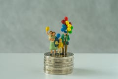 Miniature people, family holding balloon standing on stack of coins as financial business or happy retirement concept
