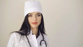 Mirada feliz del doctor bastante de sexo femenino que mira a la cámara en el fondo 4K almacen de metraje de vídeo Mirada feliz del doctor bastante de sexo femenino que mira a la cámara en el fondo 4K almacen de metraje de vídeo