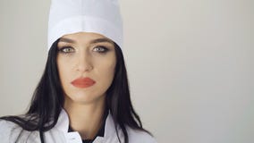 Mirada seria del doctor bastante de sexo femenino que mira a la cámara en el fondo 4K almacen de metraje de vídeo Mirada seria del doctor bastante de sexo femenino que mira a la cámara en el fondo 4K almacen de metraje de vídeo