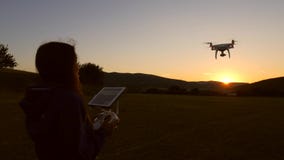 Mischrasse-Frau mit Fern-Controler steuert das fliegende Quadcopter-Brummen auf Feld während des Sonnenuntergangs HD slowmotion stock video Mischrasse-Frau mit Fern-Controler steuert das fliegende Quadcopter-Brummen auf Feld während des Sonnenuntergangs HD slowmotion stock video