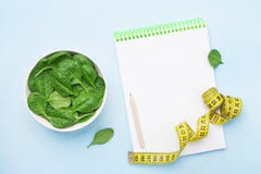 Misura verde delle foglie, del taccuino e di nastro degli spinaci sulla vista blu del piano d'appoggio Dieta e concetto sano dell immagine stock Misura verde delle foglie, del taccuino e di nastro degli spinaci sulla vista blu del piano d'appoggio Dieta e concetto sano dell immagine stock