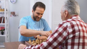 Mittlerer gealterter m?nnlicher Freiwilliger, der Schach mit ?lterem Mann im Pflegeheim, Hobby spielt stock footage Mittlerer gealterter m?nnlicher Freiwilliger, der Schach mit ?lterem Mann im Pflegeheim, Hobby spielt stock footage