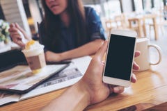 Mockup Image Of A Man`s Hand Holding White Mobile Phone With Blank Black Screen In Modern Cafe And Blur Woman Reading Newspaper Royalty Free Stock Images