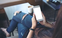 Woman`s hands holding white mobile phone with blank screen on thigh in cafe stock photos Woman`s hands holding white mobile phone with blank screen on thigh in cafe stock photos