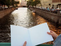 Modello del taccuino in bianco in mani femminili sui precedenti del fiume della città fotografia stock libera da diritti Modello del taccuino in bianco in mani femminili sui precedenti del fiume della città fotografia stock libera da diritti