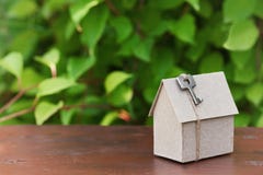 Modello della casa del cartone con la chiave contro il fondo delle foglie verdi Acquisto, affitto e concetto del bene immobile de immagini stock Modello della casa del cartone con la chiave contro il fondo delle foglie verdi Acquisto, affitto e concetto del bene immobile de immagini stock
