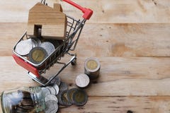 Modelo de madera de la casa en el carro de la compra con las monedas que fluyen hacia fuera del tarro de cristal Casa de compra, imagen de archivo libre de regalías Modelo de madera de la casa en el carro de la compra con las monedas que fluyen hacia fuera del tarro de cristal Casa de compra, imagen de archivo libre de regalías