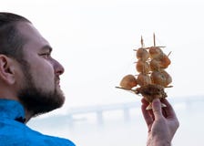 Modelo de navio com as conchas do mar na mão farpada do homem na frente do rio imagens de stock Modelo de navio com as conchas do mar na mão farpada do homem na frente do rio imagens de stock