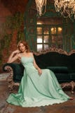 Modelo luxuoso da mulher em um vestido hortelã-colorido que senta-se em um sofá do vintage Menina da beleza com uma composição e imagem de stock Modelo luxuoso da mulher em um vestido hortelã-colorido que senta-se em um sofá do vintage Menina da beleza com uma composição e imagem de stock