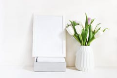 Modelo vazio branco do quadro de madeira com o ramalhete da mola das tulipas no vaso da porcelana e a pilha dos livros que encont imagens de stock Modelo vazio branco do quadro de madeira com o ramalhete da mola das tulipas no vaso da porcelana e a pilha dos livros que encont imagens de stock