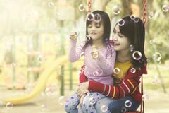 Moder och dotter som har gyckel med såpbubblor på lekplatsen arkivbilder Moder och dotter som har gyckel med såpbubblor på lekplatsen arkivbilder