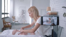 Moderlig omsorg, mammavlogger undervisar hur man ändrar den nyfödda ungen för kläder, medan anteckna utbildningsvideoen på mobilt arkivfilmer Moderlig omsorg, mammavlogger undervisar hur man ändrar den nyfödda ungen för kläder, medan anteckna utbildningsvideoen på mobilt arkivfilmer
