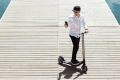 Modern man dressed white shirt and black pants using his phone while standing at a wooden pier with electric scooter stock photography Modern man dressed white shirt and black pants using his phone while standing at a wooden pier with electric scooter stock photography