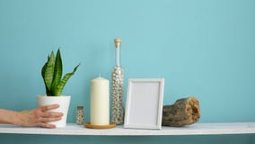 Modern room decoration with picture frame mockup. White shelf against pastel turquoise wall with candle and rocks in bottle. Hand stock video Modern room decoration with picture frame mockup. White shelf against pastel turquoise wall with candle and rocks in bottle. Hand stock video