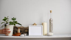 Modern rumgarnering med modellen för bildram Hyllan mot den vita väggen med den dekorativa stearinljuset, exponeringsglas och v Modern rumgarnering med modellen för bildram Hyllan mot den vita väggen med den dekorativa stearinljuset, exponeringsglas och v