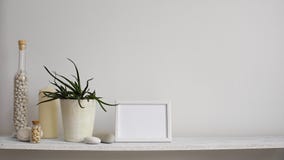 Modern rumgarnering med modellen för bildram Hyllan mot den vita väggen med den dekorativa stearinljuset, exponeringsglas och v Modern rumgarnering med modellen för bildram Hyllan mot den vita väggen med den dekorativa stearinljuset, exponeringsglas och v