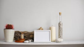 Modern rumgarnering med modellen för bildram Hyllan mot den vita väggen med den dekorativa stearinljuset, exponeringsglas och v Modern rumgarnering med modellen för bildram Hyllan mot den vita väggen med den dekorativa stearinljuset, exponeringsglas och v