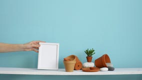 Modern rumgarnering med modellen för ram för handinnehavbild Vit hylla mot den pastellfärgade turkosväggen med krukmakeri och Modern rumgarnering med modellen för ram för handinnehavbild Vit hylla mot den pastellfärgade turkosväggen med krukmakeri och