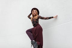 Modern Sexy Young Woman In Fashionable Clothes In Stylish Purple Hat In Leather Shoes Is Posing Near A Vintage White Wall Outdoors Stock Images Modern Sexy Young Woman In Fashionable Clothes In Stylish Purple Hat In Leather Shoes Is Posing Near A Vintage White Wall Outdoors Stock Images
