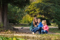 Modern spelar med hennes dotter, och sonen i parkerar vid dammet arkivfoto Modern spelar med hennes dotter, och sonen i parkerar vid dammet arkivfoto