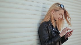 Modieus jong en mooi meisje met een smartphone in handen Het meisje bekijkt het telefoonscherm Tegen a stock video Modieus jong en mooi meisje met een smartphone in handen Het meisje bekijkt het telefoonscherm Tegen a stock video