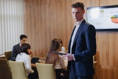Modieuze jonge zakenman die een jasje en een overhemd op de achtergrond van een werkend bureau met mensen dragen die met een tabl royalty-vrije stock fotografie Modieuze jonge zakenman die een jasje en een overhemd op de achtergrond van een werkend bureau met mensen dragen die met een tabl royalty-vrije stock fotografie