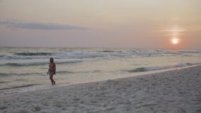 Modieuze zwangere vrouw die in swimsuite op een zandig strand langs overzeese golven op zonsondergang 4k lopen stock footage Modieuze zwangere vrouw die in swimsuite op een zandig strand langs overzeese golven op zonsondergang 4k lopen stock footage