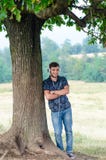 Modischer Jugendlicher sitzen nahe einem Baum hören Musik in der Natur lizenzfreie stockfotografie Modischer Jugendlicher sitzen nahe einem Baum hören Musik in der Natur lizenzfreie stockfotografie