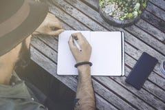Modnisia męski uczeń robi notatkom, pisze celach w notepad podczas gdy siedzący na tarasie kawiarnia Skoncentrowany mężczyzna wri zdjęcie royalty free Modnisia męski uczeń robi notatkom, pisze celach w notepad podczas gdy siedzący na tarasie kawiarnia Skoncentrowany mężczyzna wri zdjęcie royalty free