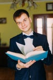 Modny młody człowiek trzyma książkę i patrzeje kamerę z krawatem Pokój hotelowy w tle fotografia royalty free Modny młody człowiek trzyma książkę i patrzeje kamerę z krawatem Pokój hotelowy w tle fotografia royalty free