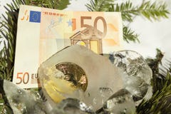 Moeda de ouro de Bitcoin congelada ao meio em uma parte de gelo em um fundo branco com ramos de árvore do Natal e no euro 50 de E fotografia de stock Moeda de ouro de Bitcoin congelada ao meio em uma parte de gelo em um fundo branco com ramos de árvore do Natal e no euro 50 de E fotografia de stock