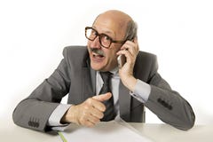 Mogen hög affärsman som talar på mobiltelefonen på att arbeta för kontorsskrivbord som är lyckligt, och att göra en gest som är r royaltyfri bild Mogen hög affärsman som talar på mobiltelefonen på att arbeta för kontorsskrivbord som är lyckligt, och att göra en gest som är r royaltyfri bild