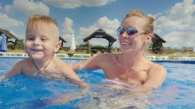 Mom and the baby boy swim in the pool. Have fun together. Slow motion 10 bit video